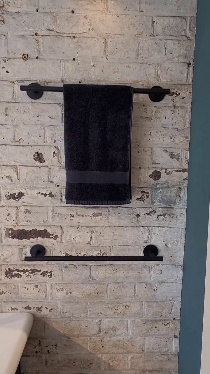 Matte black towel rail with black towel against exposed brick wall in an industrial-style bathroom.