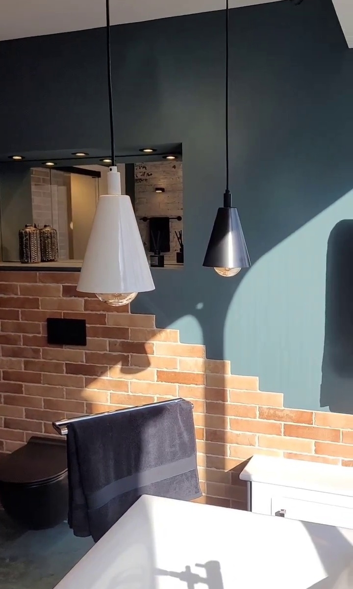Bathroom with black and white pendant lights, black towel rail with towel, exposed brick wall, and freestanding bathtub corner