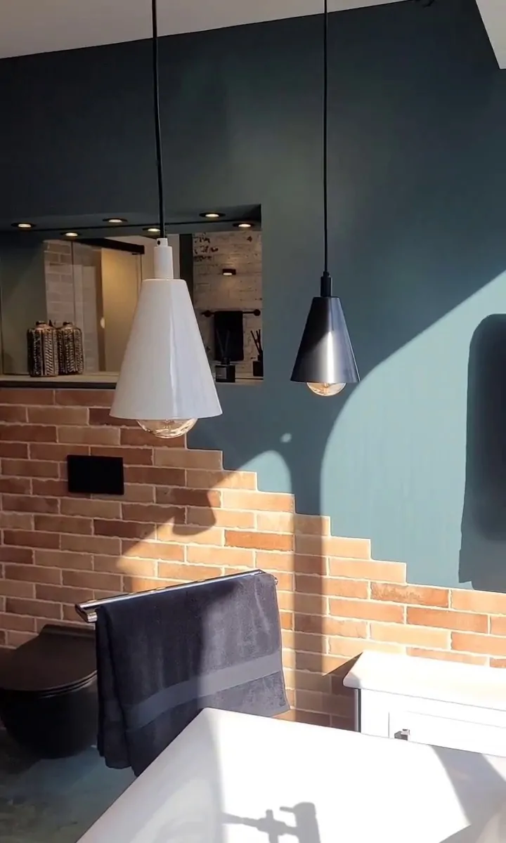 Bathroom with black and white pendant lights, black towel rail with towel, exposed brick wall, and freestanding bathtub corner