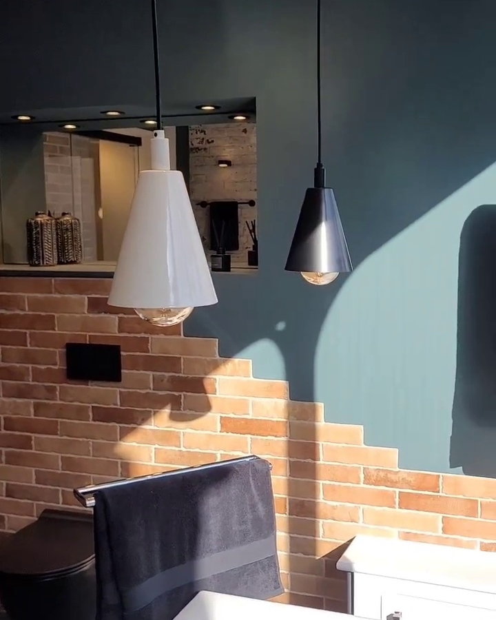 Bathroom with black and white pendant lights, black towel rail with towel, exposed brick wall, and freestanding bathtub corner