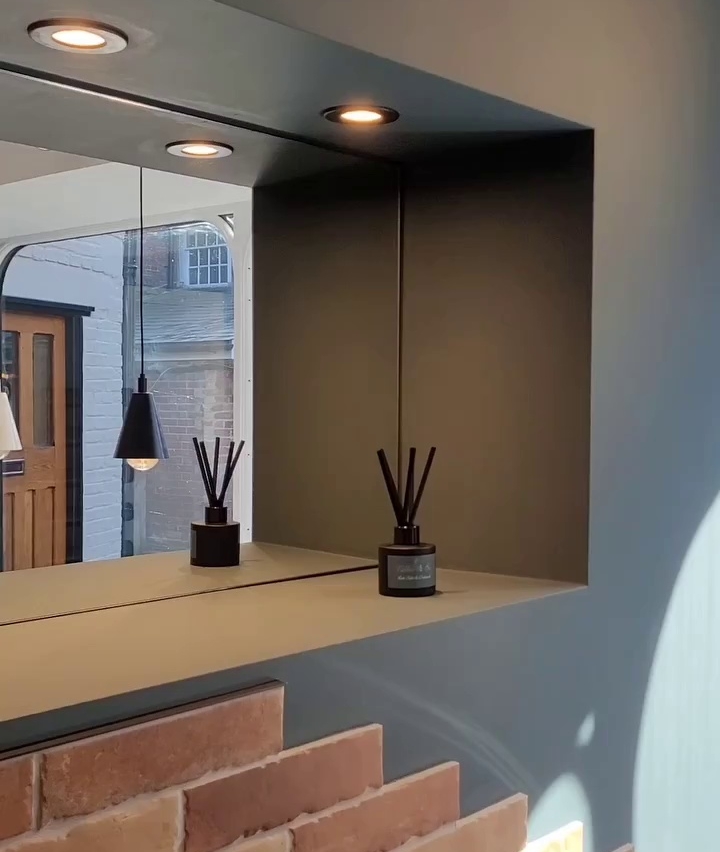 Bathroom mirror with built-in lights, black pendant light, and reed diffuser, above brick half-wall.