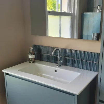 Floating blue vanity unit under sash window with mirror