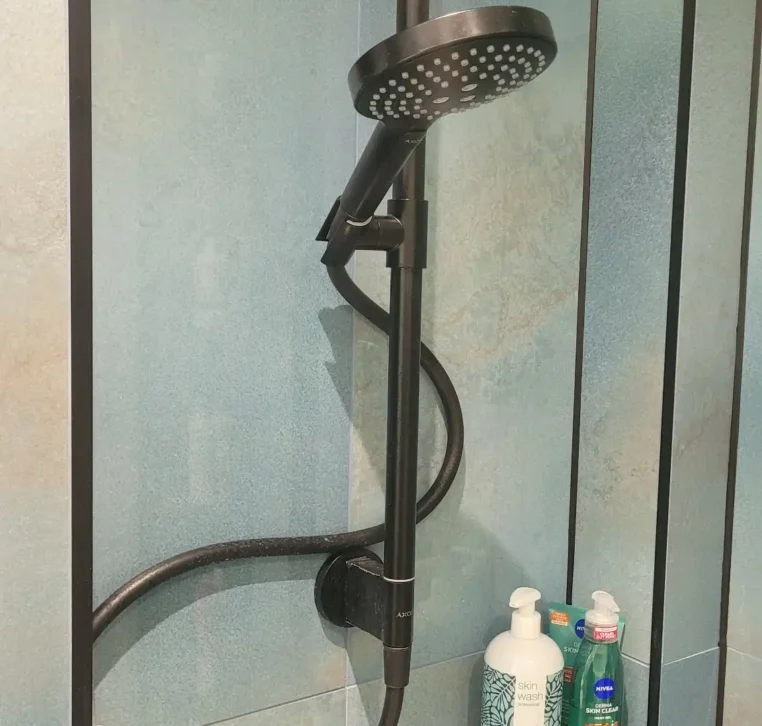 Close-up of modern black shower fitting on blue wall.