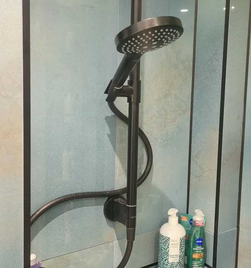 Close-up of modern black shower fitting on blue wall.