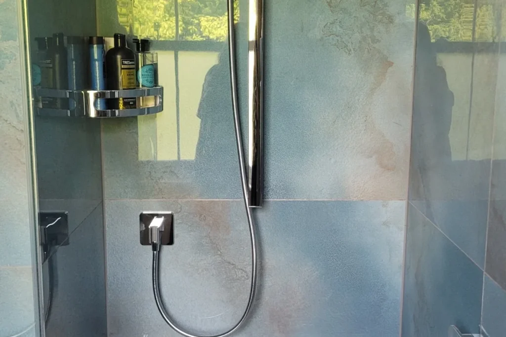Modern walk-in shower with rainfall head, handheld spray and built-in bench on blue tiles.
