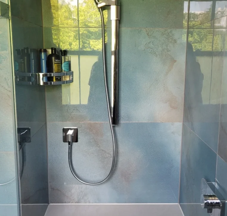 Modern walk-in shower with rainfall head, handheld spray and built-in bench on blue tiles.