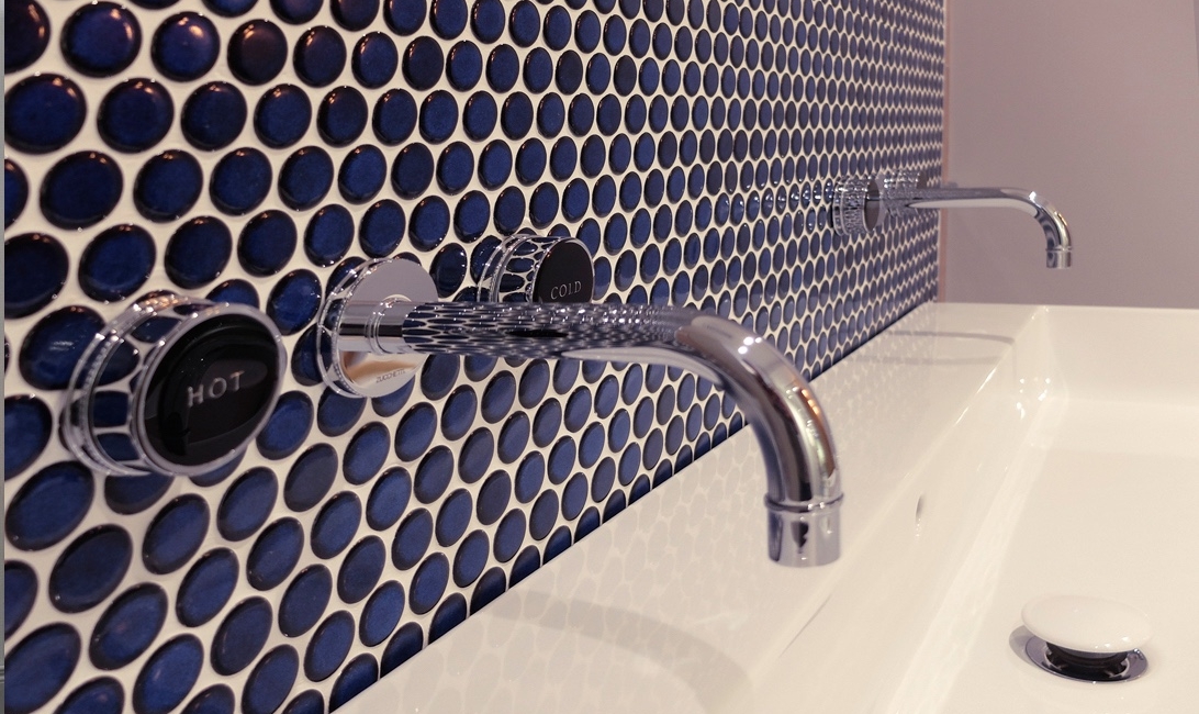 Dark blue tiles behind a sink with a hot and cold tap