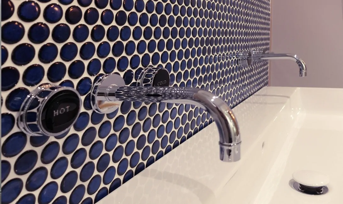 Dark blue tiles behind a sink with a hot and cold tap
