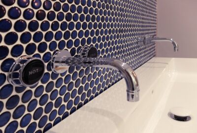 Dark blue tiles behind a sink with a hot and cold tap