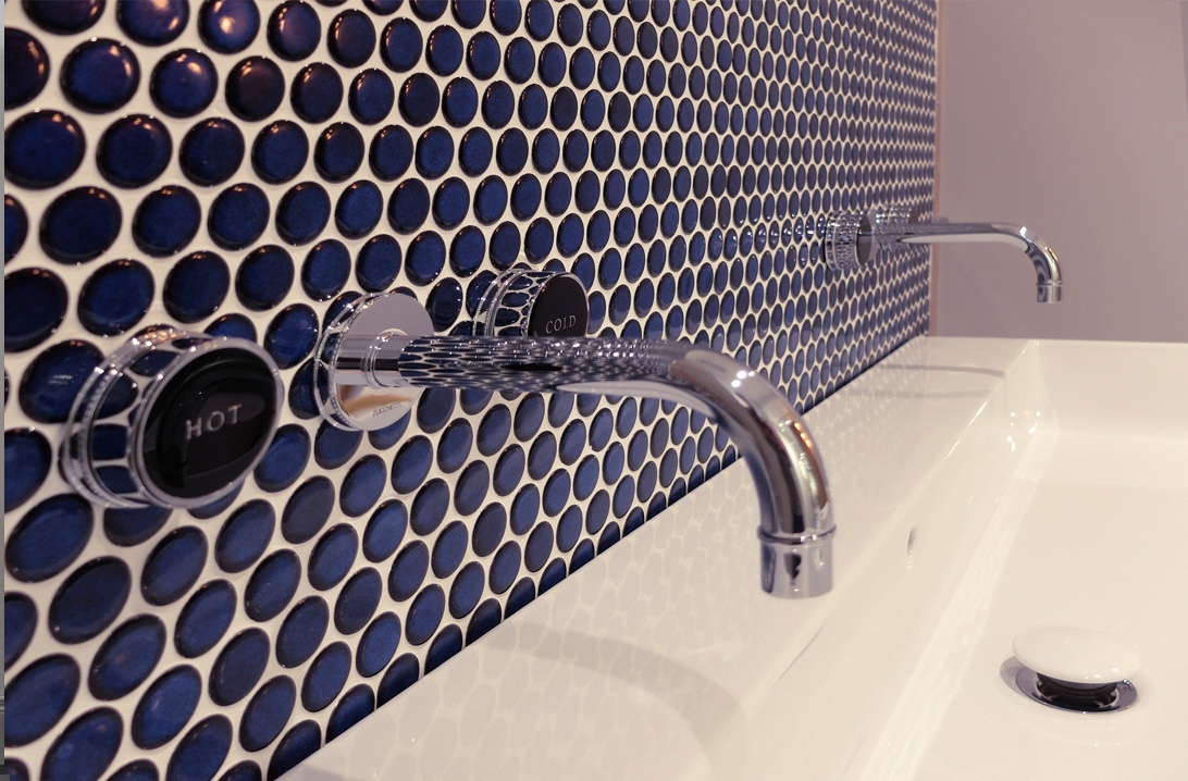 Dark blue tiles behind a sink with a hot and cold tap