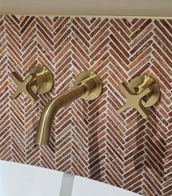 Brushed brass wall-mounted taps against decorative herringbone tiles