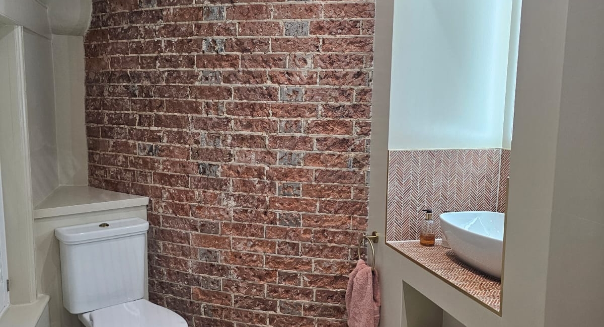 Light-filled wet room with exposed oast brickwork, wall-hung toilet and walk-in shower