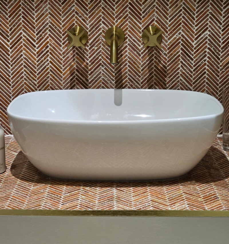 Freestanding white bath set against patterned tiles and original exposed brickwork