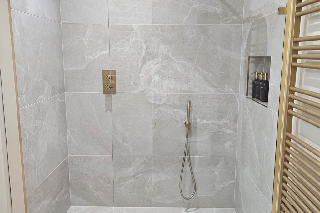 Walk-in shower with marble-effect tiles, glass screen and brass fittings