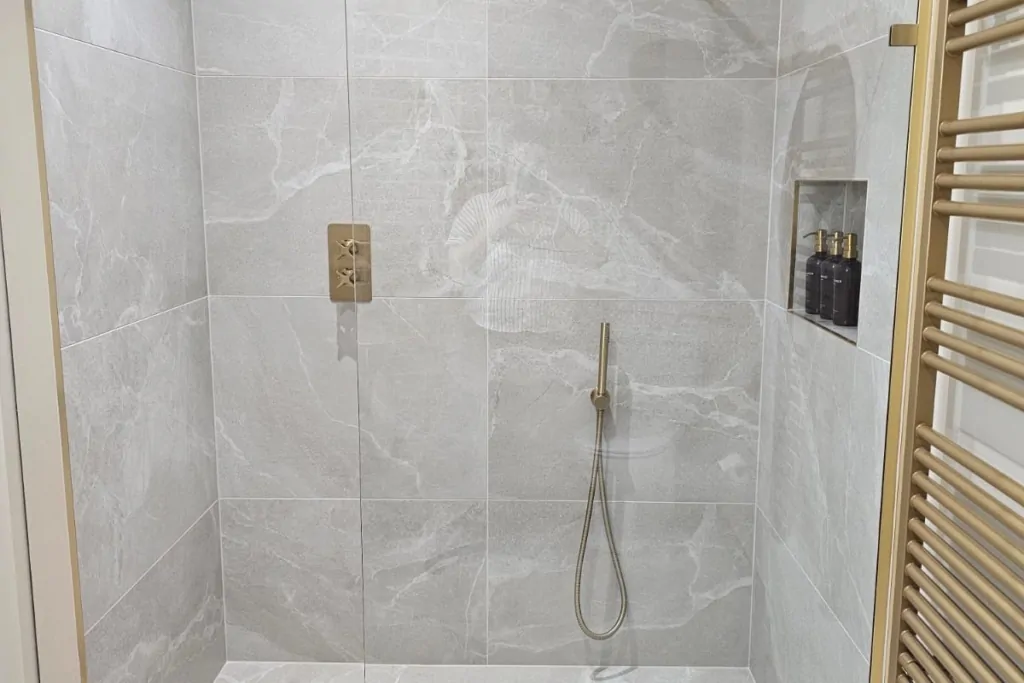 Walk-in shower with marble-effect tiles, glass screen and brass fittings