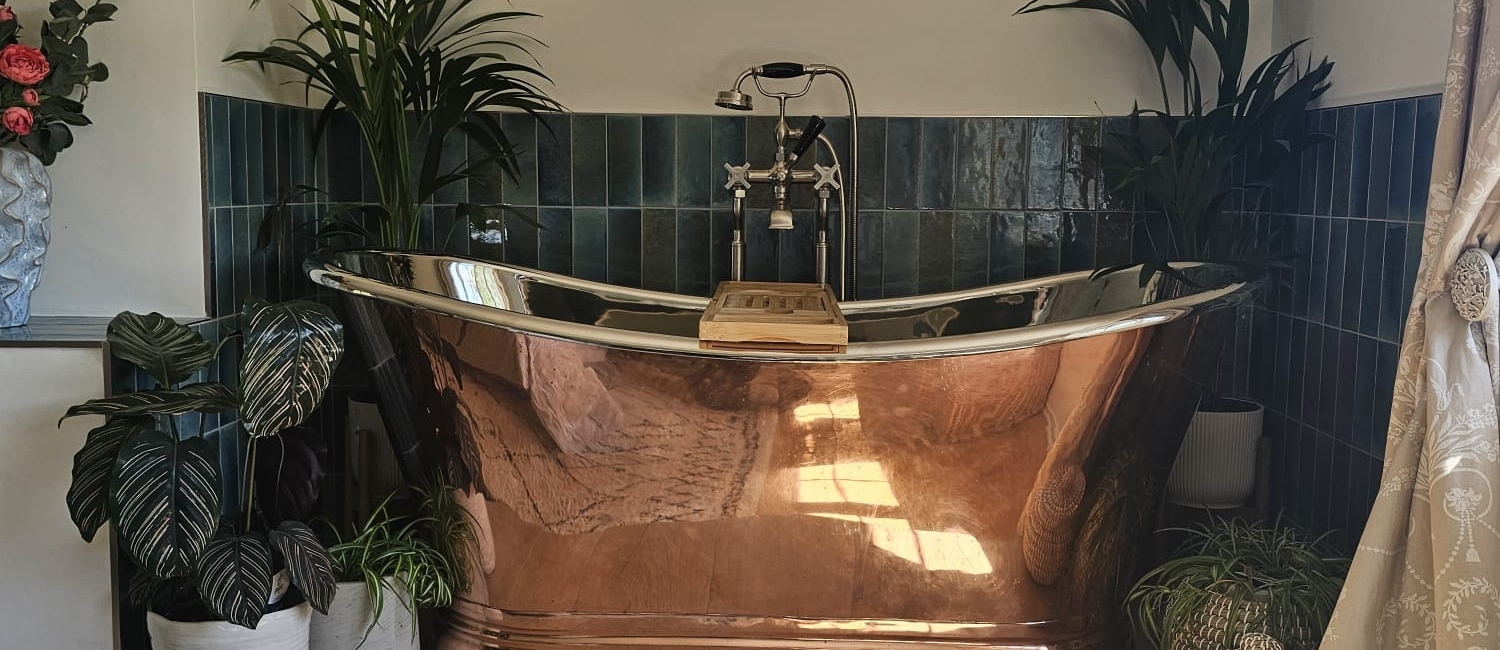 Copper and nickel freestanding bath surrounded by botanical plants and blue tiled walls