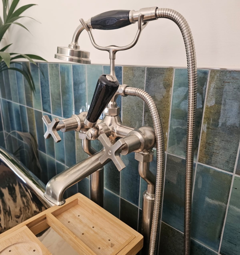 Traditional freestanding bath filler with hand shower beside blue glazed wall tiles