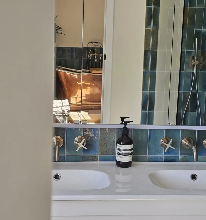 White basin with mirrored storage, brushed brass fittings and blue tiled splashback