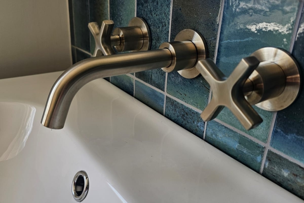 White basin with brushed brass wall-mounted tap and blue tiled splashback