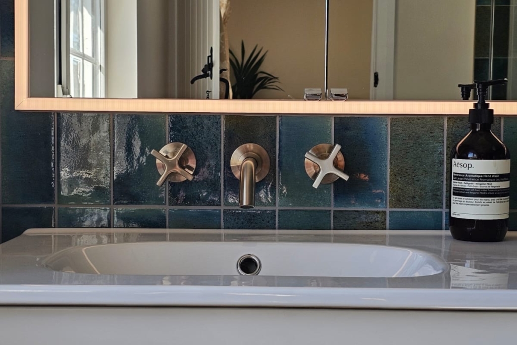 White vanity unit with basin, illuminated mirror and brushed brass fittings
