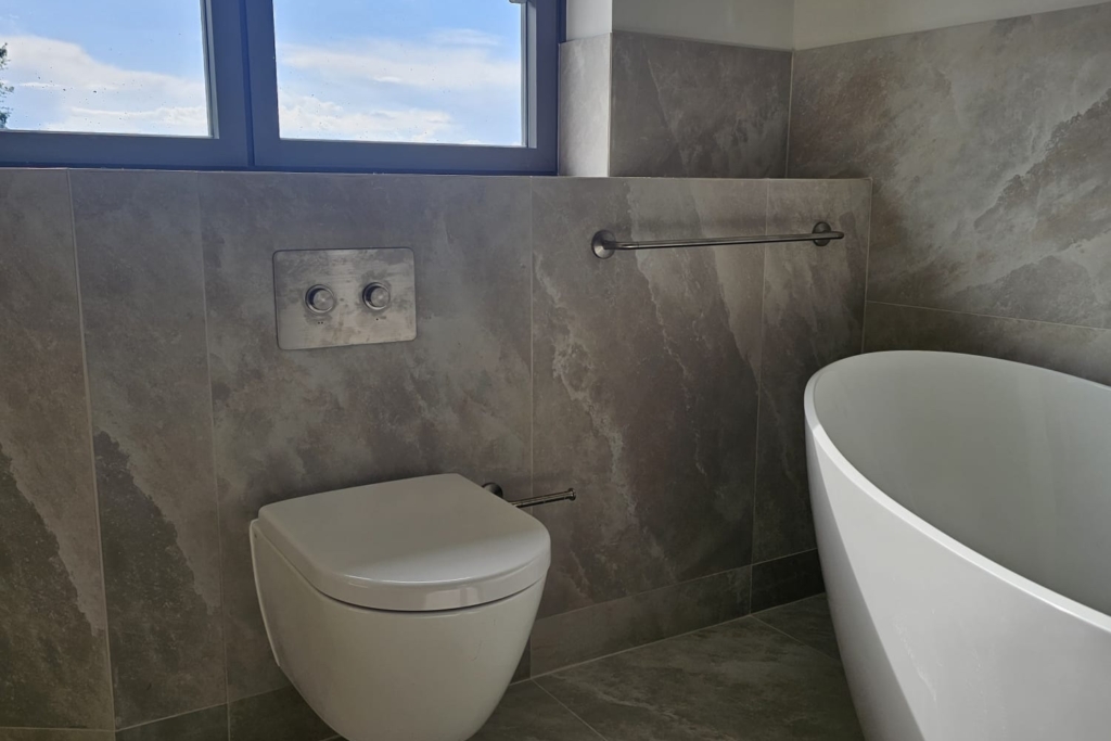 Wall-hung toilet beside a freestanding bath beneath a bathroom window