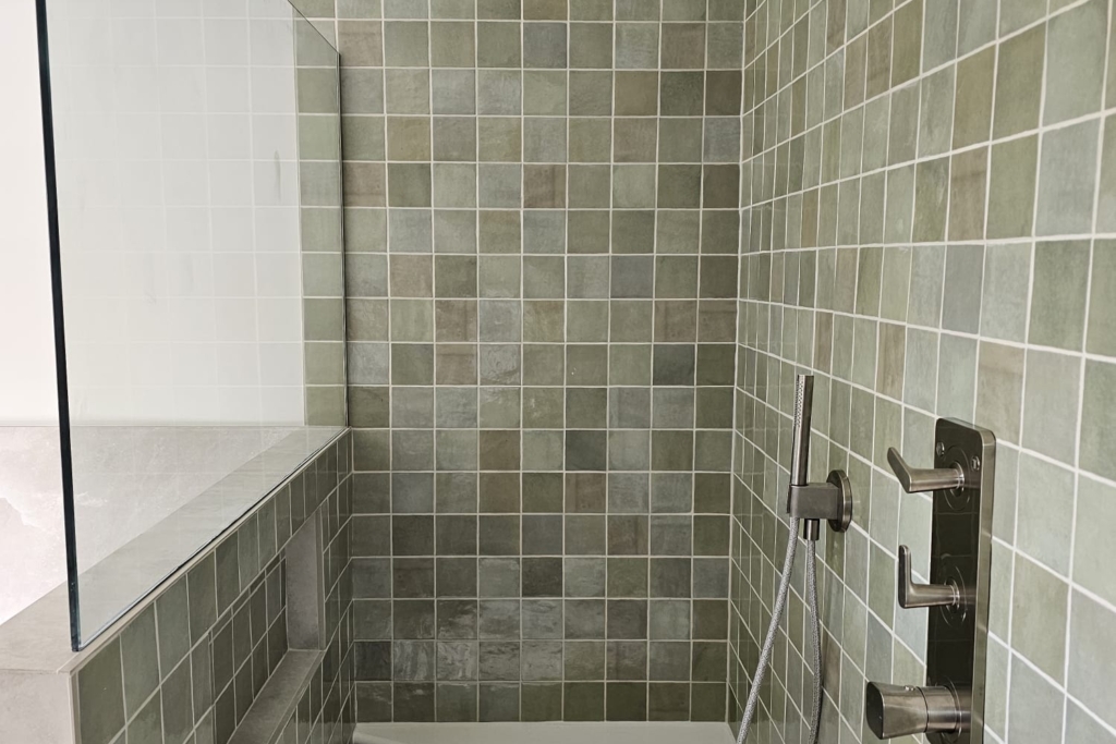 Walk-in shower with green textured tiles, glass screen and built-in bench
