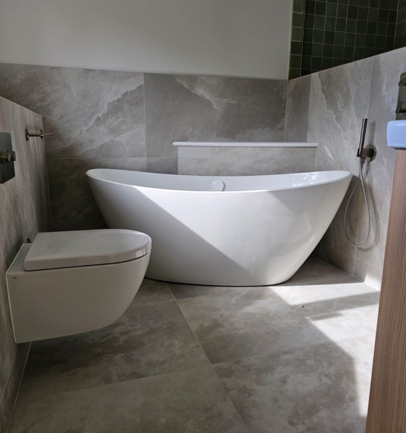 Freestanding white bath set against large-format stone-effect wall tiles