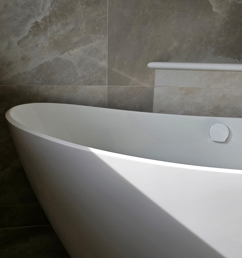 Close-up of a freestanding white bath with stone-effect tiled surround