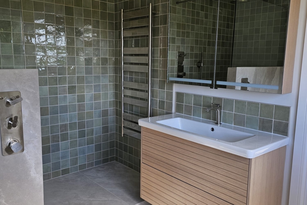 Floating wood-effect vanity with basin beside a green tiled walk-in shower