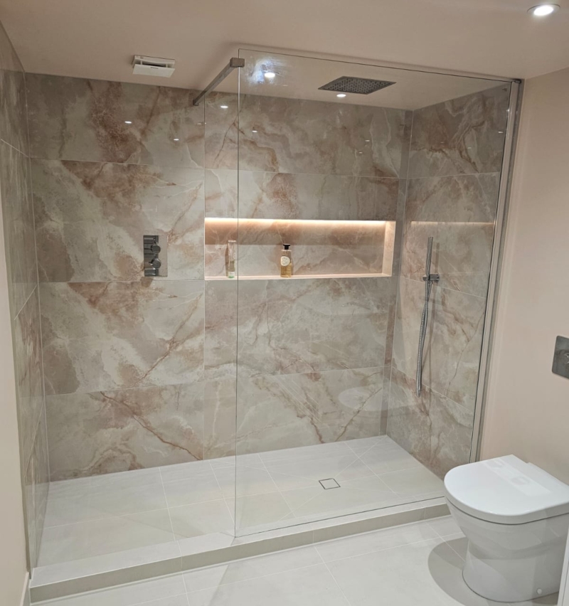 Walk-in wet room shower with marble-effect tiles and recessed illuminated shelf