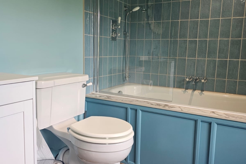 Traditional toilet and blue fitted bath with panelled cabinetry