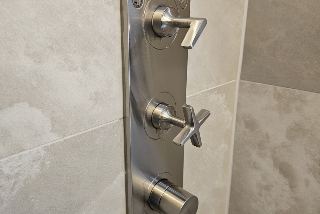 Chrome shower control mounted on grey stone-effect bathroom tiles