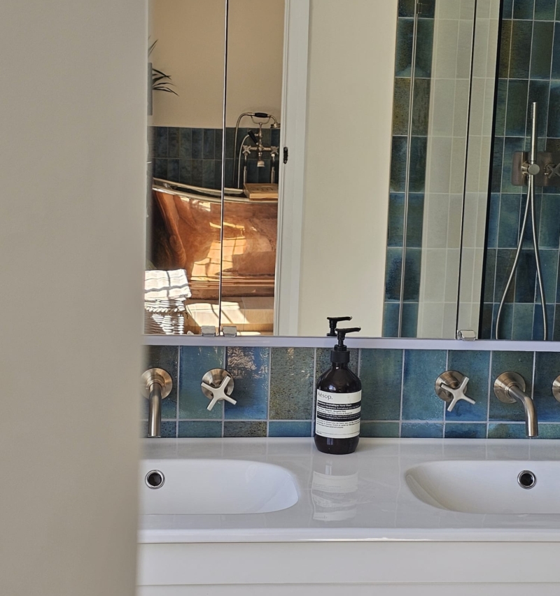 White bathroom basin with mirrored storage and blue tiled splashback