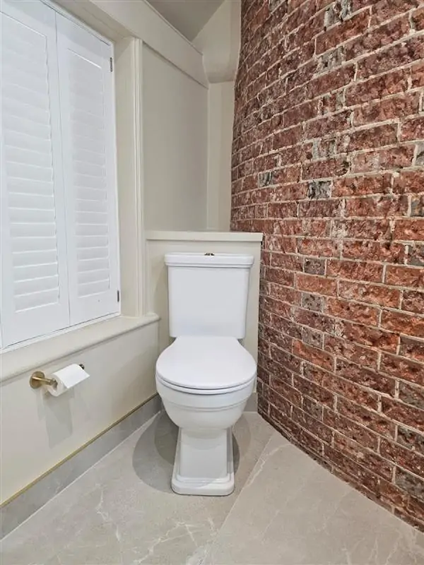 Wall-hung toilet beside exposed brickwork in a bright wet room